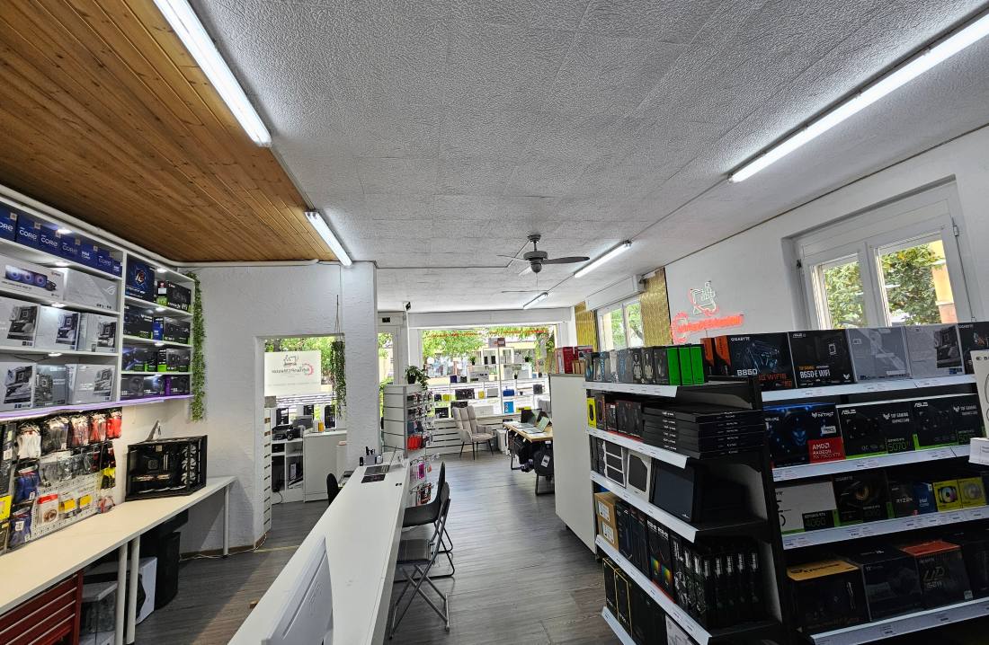 Intérieur du magasin AdrianPCMaster, Avenue du Marché 8 à Sierre : l'allée centrale, les rayonnages de composants et de périphériques, les machines exposées.