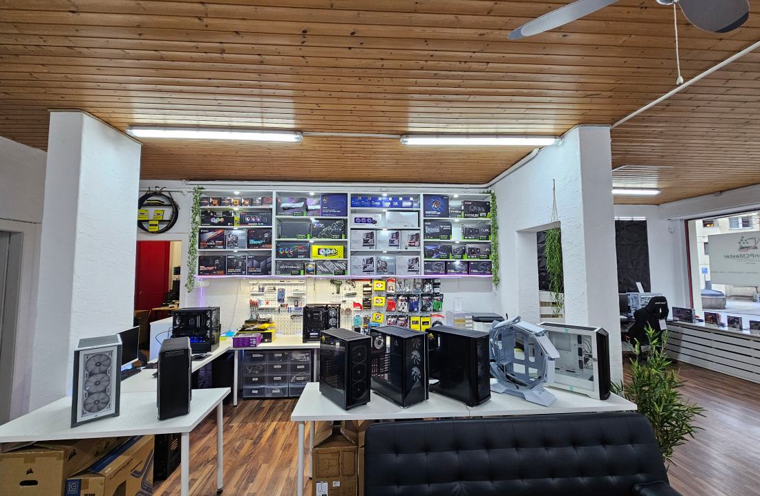 Le magasin AdrianPCMaster de Sierre vu de l'intérieur : plafond en bois, boîtiers exposés sur les tables, mur de composants et coin d'attente.